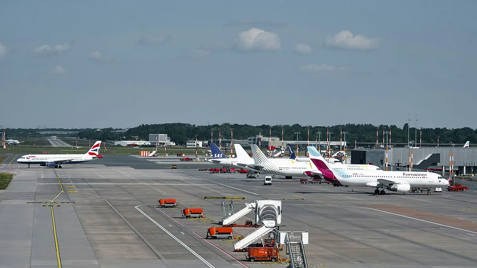 Airplane taxiing on airport runway with several planes parked nearby. Clear sky, airport terminals in background.