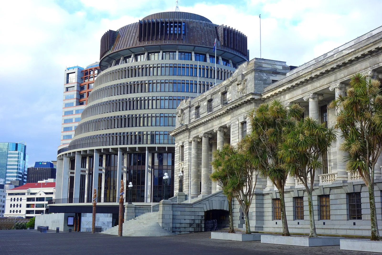 The Beehive and the colonnaded Parliament House in Wellington, with cabbage trees in front